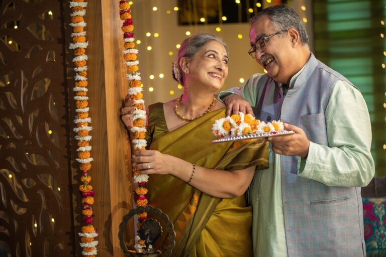 Senior woman hanging floral garlands at entrance while decorating house with husband during Diwali festival